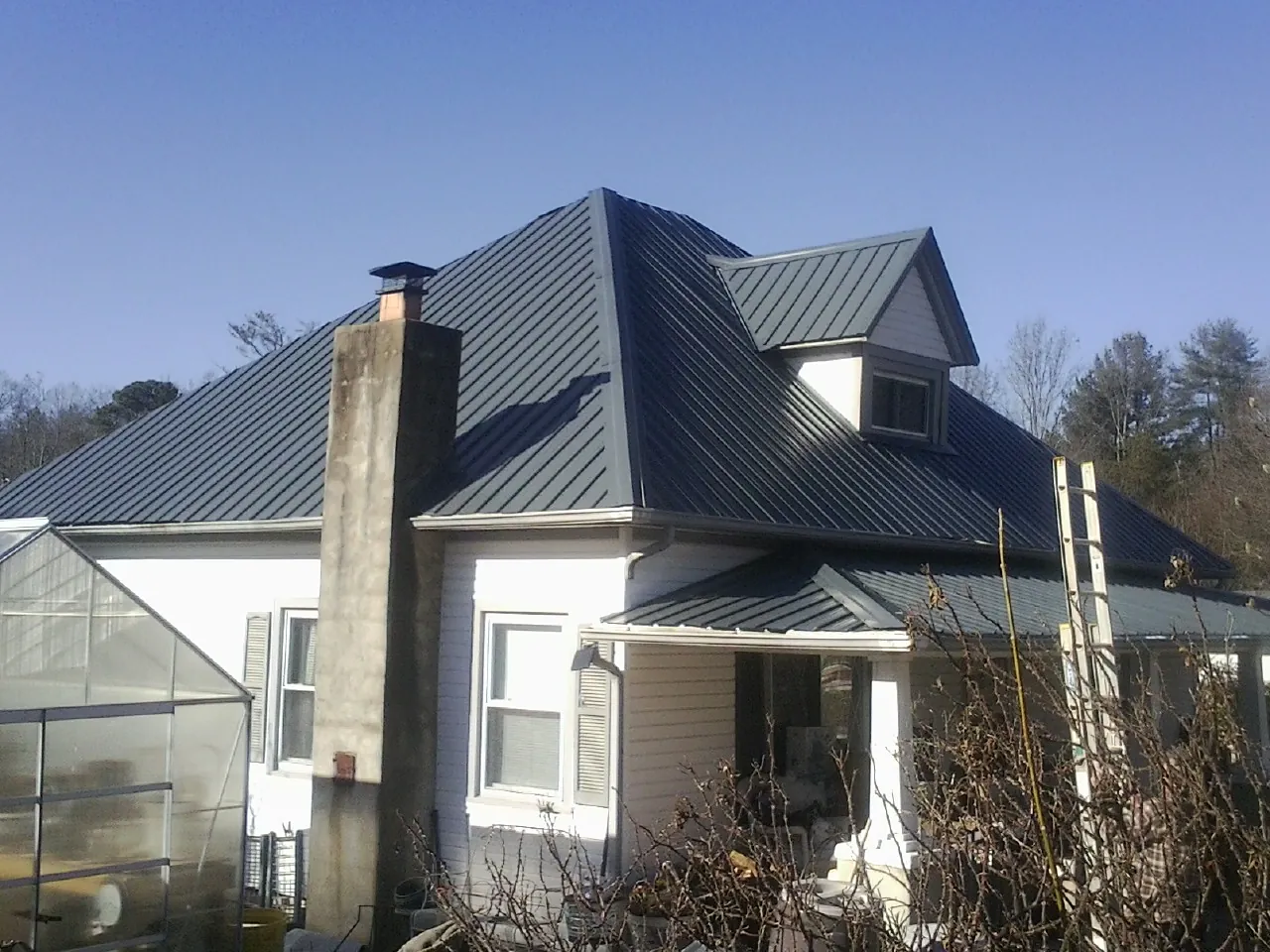 Dark blue standing seam metal roof on a white farmhouse with dormer — Slate & Tile Roof Repair by Roofing Brothers in De Ruyter