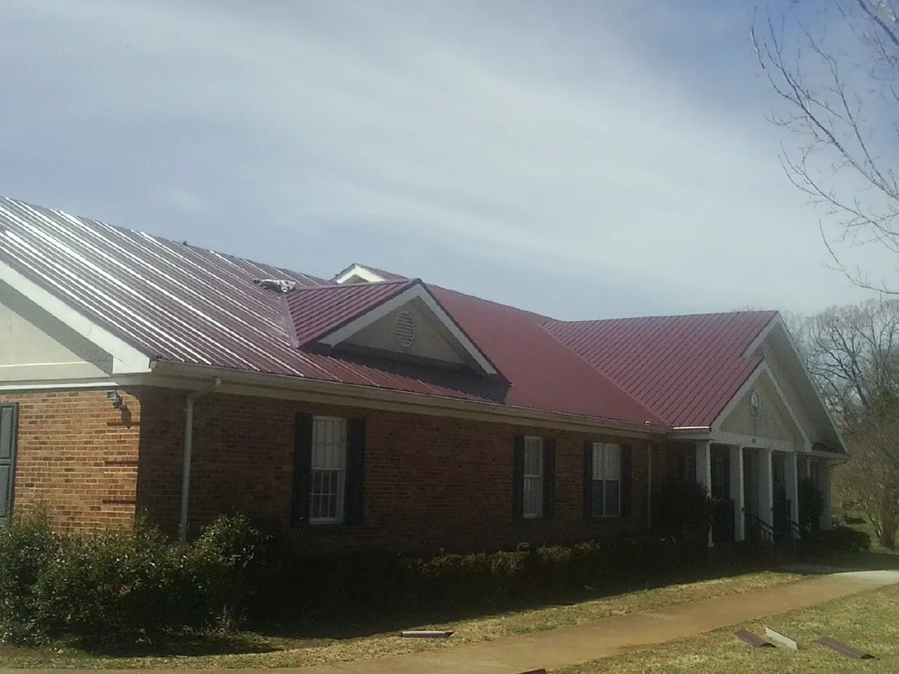 Red metal roof with gabled entries on a long brick building, from a Hail Damage Roof Repair job in De Ruyter