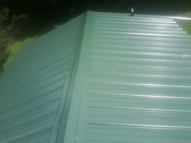 New green metal panels meeting at the ridge of a roof — Flat Roof Repair work by our crew in De Ruyter
