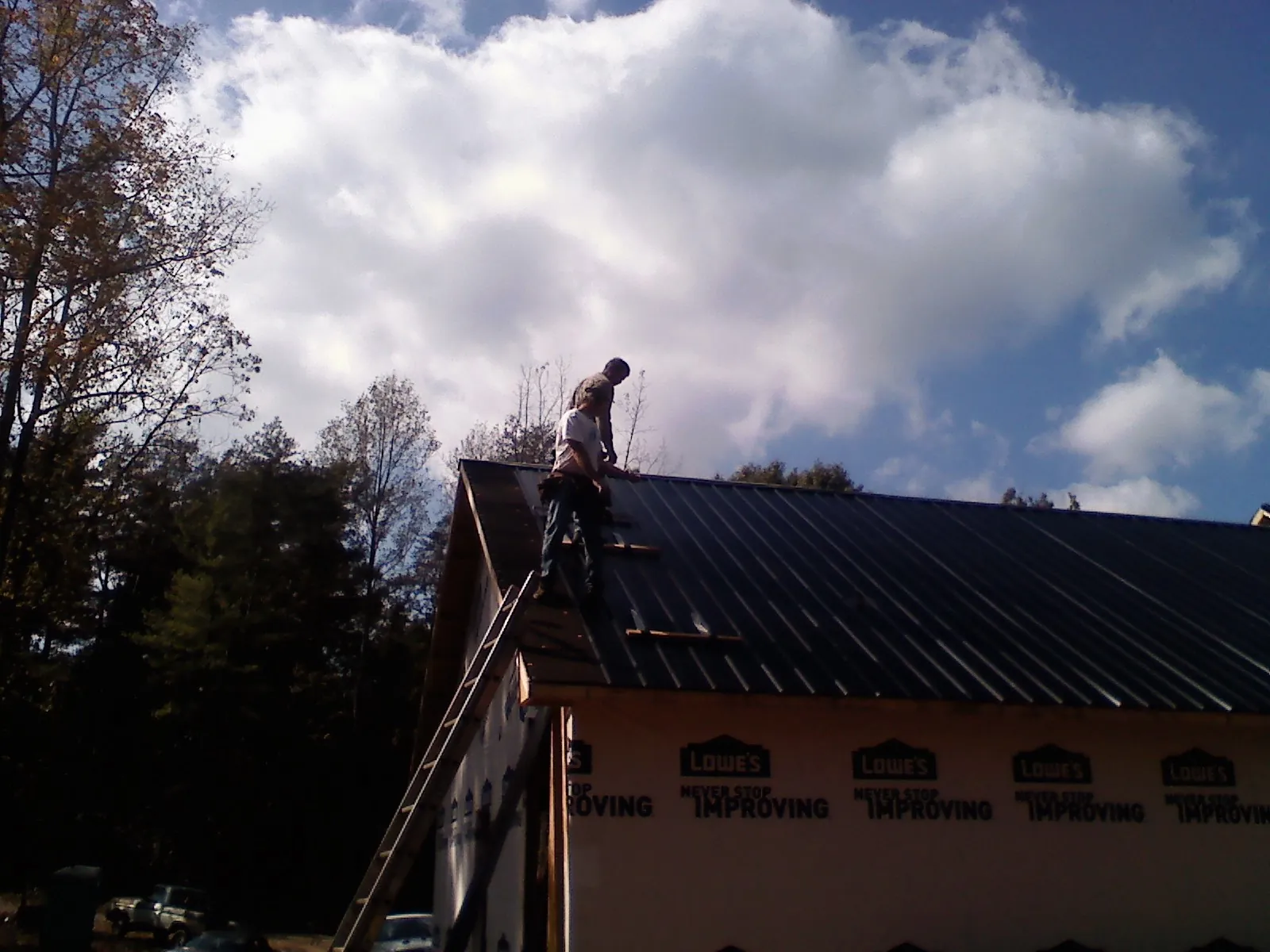 Roofer fastening dark metal panels high against a cloudy sky, from a Roof Inspection job in De Ruyter
