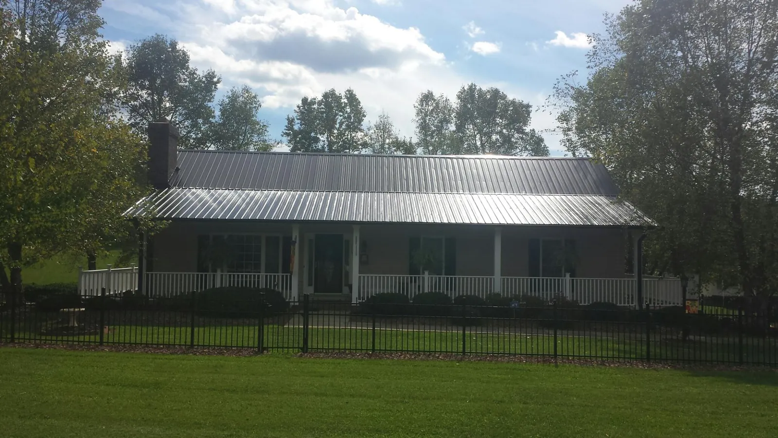 Gray metal roof on a brick ranch with a full width front porch — Gutter Guard Installation work by our crew in De Ruyter
