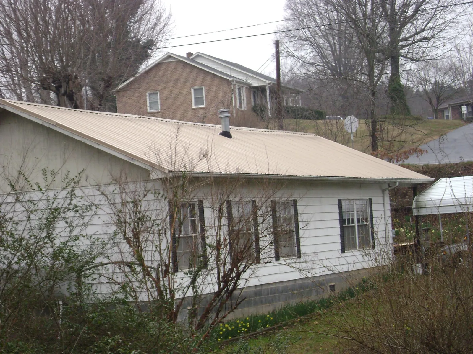 Tan metal roof on a white sided house set into a hillside — Commercial Roofing by Roofing Brothers in De Ruyter